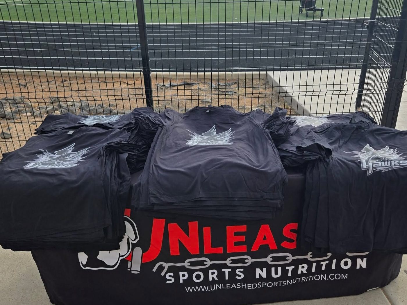 Stacked sponsored team shirts on the Unleashed table at the track